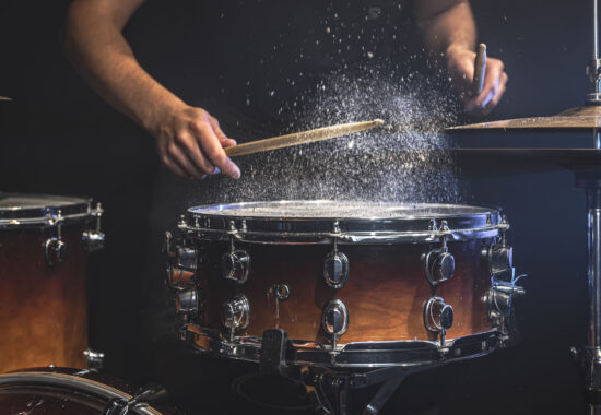 A male drummer plays snare drum with drumsticks in a dark room.