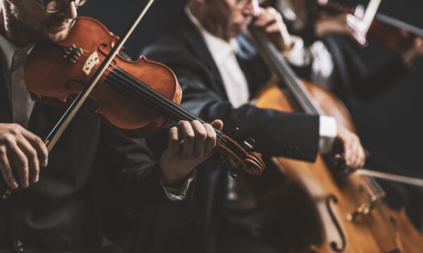 Professional symphonic string orchestra performing on stage and playing a classical music concert, violinist in the foreground